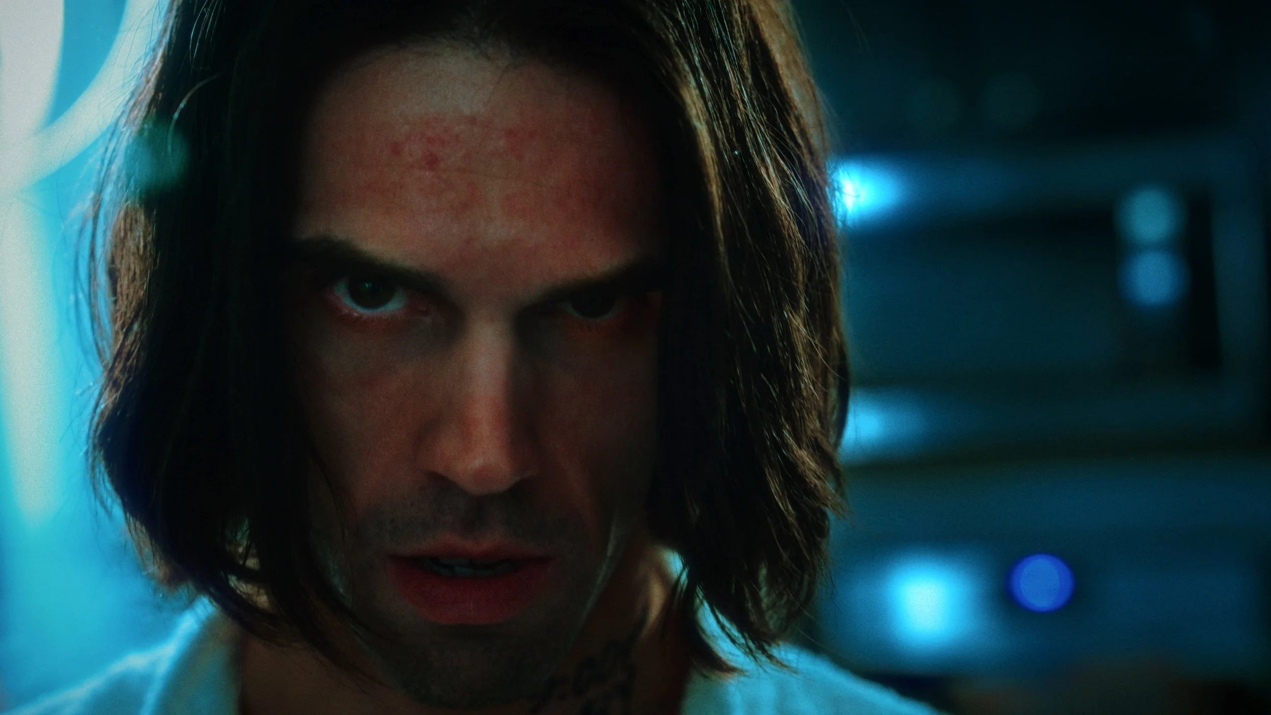 Tom staring directly into camera in a blue-lit room